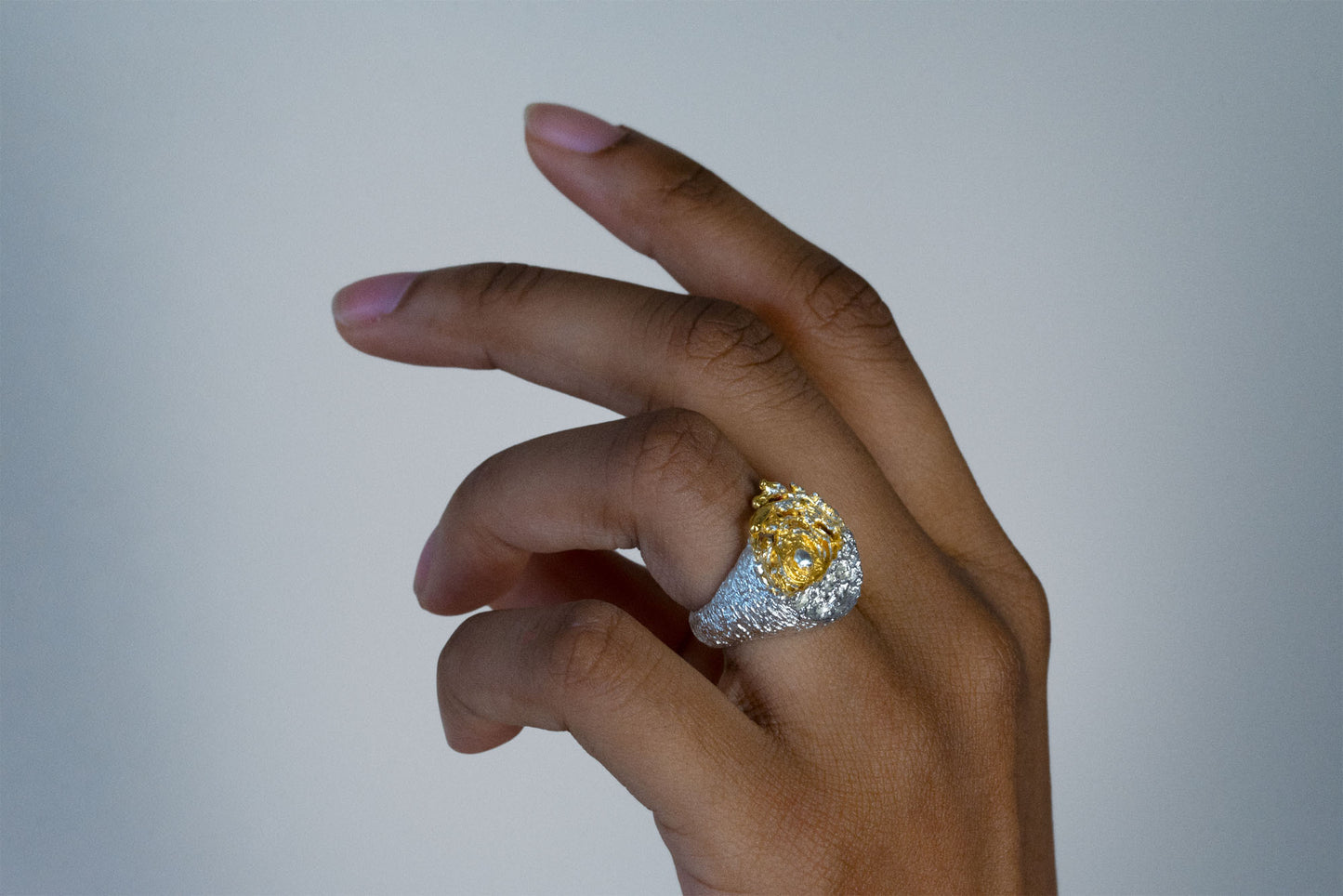 A close-up of a hand wearing a large statement sea silver ring with a yellow center with a white sun and a textured silver band, set against a dark navy ribbed sweater.