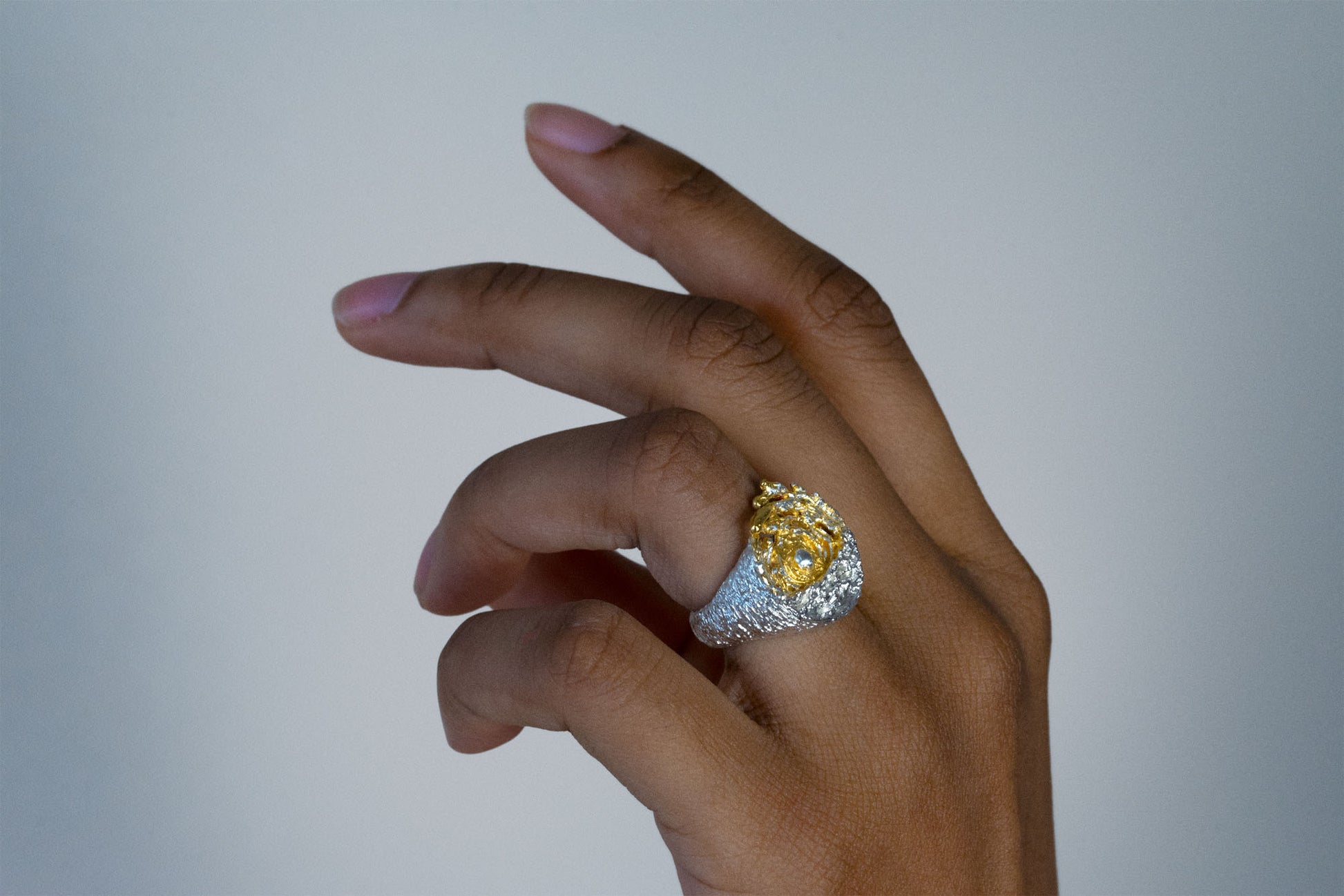 A close-up of a hand wearing a large statement sea silver ring with a yellow center with a white sun and a textured silver band, set against a dark navy ribbed sweater.