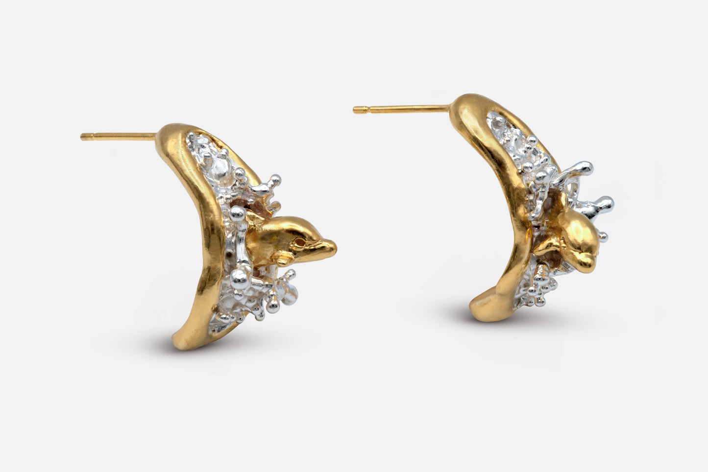 A pair of sculptural gold vermeil and silver earrings featuring two dolphins leaping out of the sea, mid-splash. 