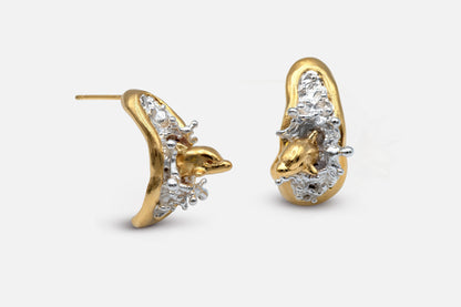 A pair of sculptural gold vermeil and silver earrings featuring two dolphins leaping out of the sea, mid-splash. 