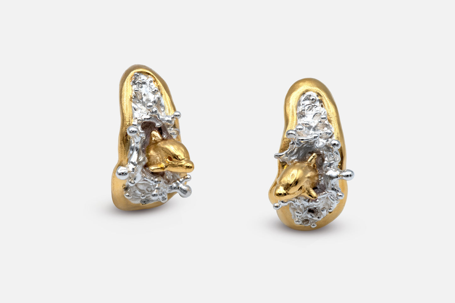 A pair of sculptural gold vermeil and silver earrings featuring two dolphins leaping out of the sea, mid-splash. 