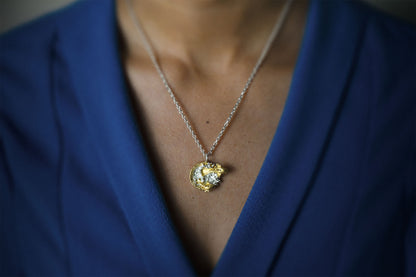 A close-up shot of a person wearing a delicate gold pendant necklace with a clear crystal center, styled against a royal blue blazer.