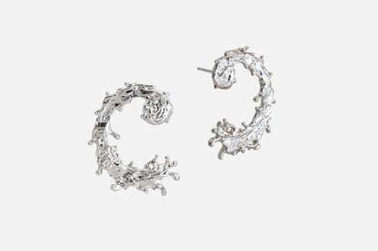 A pair of silver earrings with a textured, organic design like the waters of the sea swirling in a circular pattern, displayed on a clean light gray background.
