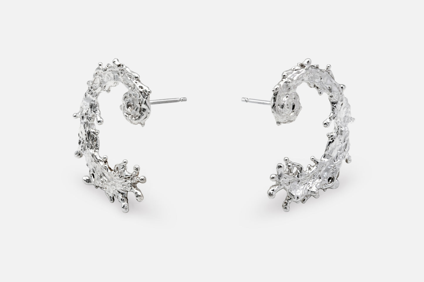 A pair of silver earrings with a textured, organic design like the waters of the sea swirling in a circular pattern, displayed on a clean light gray background.