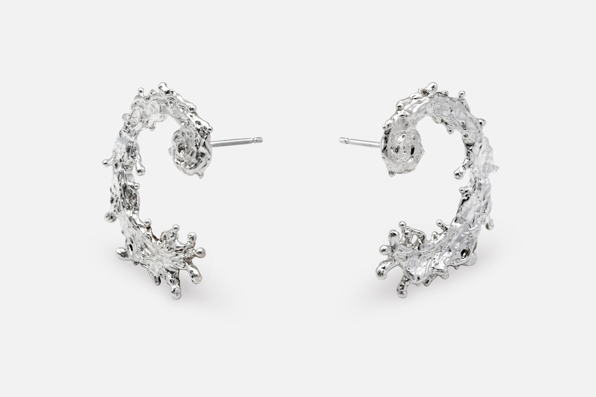 A pair of silver earrings with a textured, organic design like the waters of the sea swirling in a circular pattern, displayed on a clean light gray background.