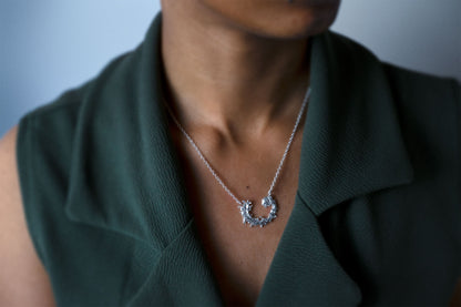 Woman wearing a silver necklace featuring a textured, organic crescent moon pendant with a design like the waters of the sea swirling in a circular pattern, set against a dark green jacket.