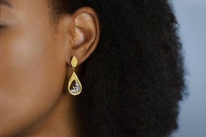 A close-up side profile of a person with dark curly hair wearing a pair of gold vermeil and silver teardrop dangle earrings with a textured, ribbed gold top and a water shaped silver center.