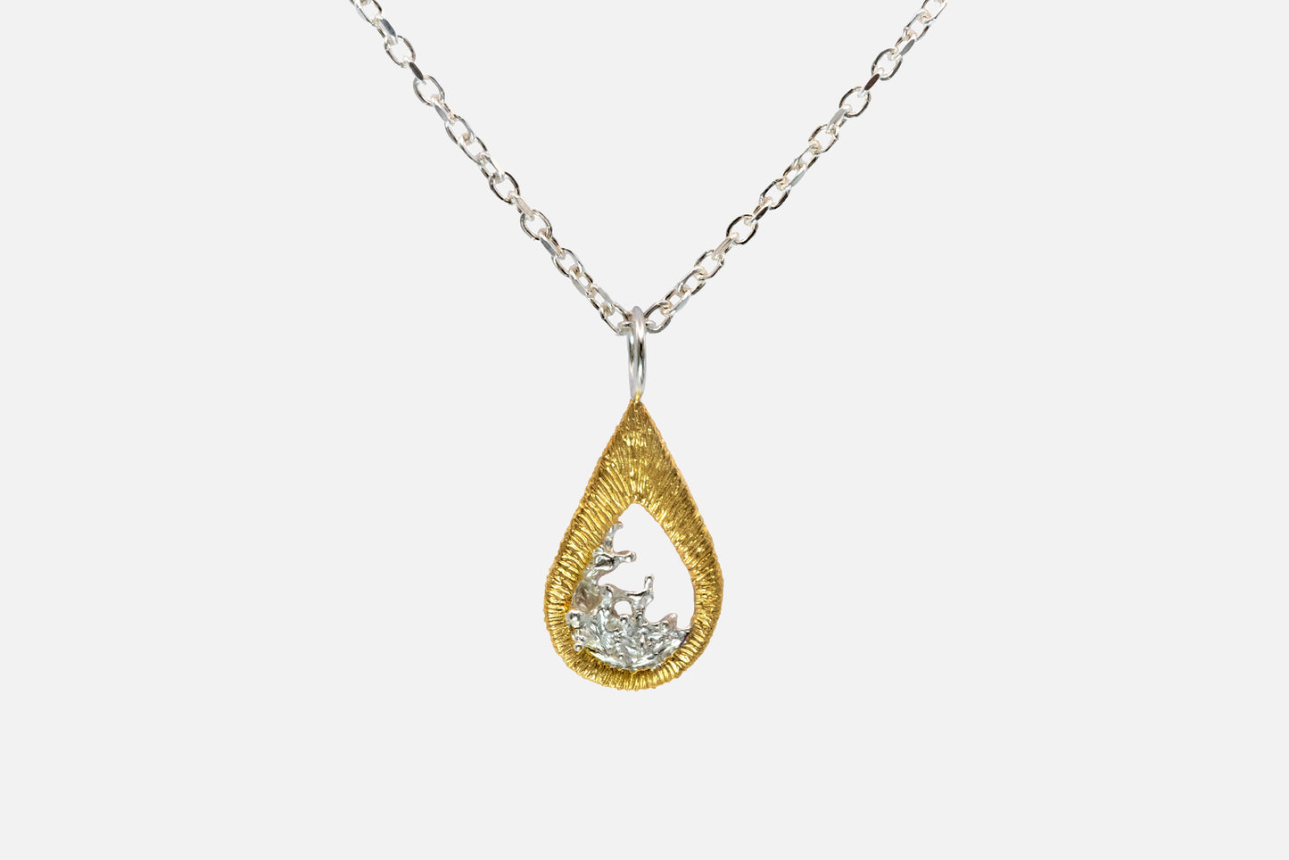 A teardrop-shaped gold vermeil and silver pendant necklace featuring a textured gold outer frame and a silver-toned inner design shaped like moving water, suspended from a silver chain against a light gray background.