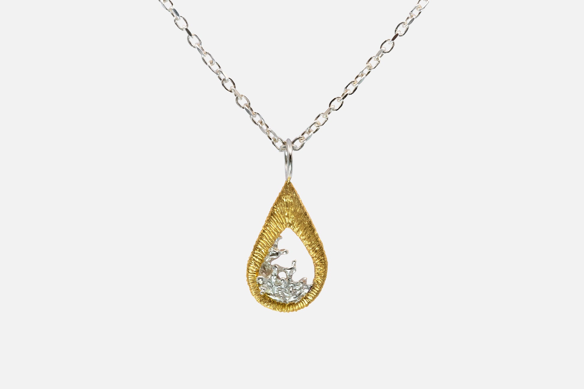 A teardrop-shaped gold vermeil and silver pendant necklace featuring a textured gold outer frame and a silver-toned inner design shaped like moving water, suspended from a silver chain against a light gray background.