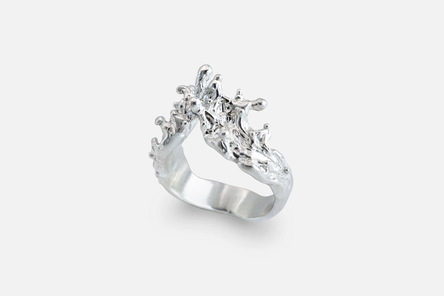 A silver ring with a sculptural, textured top, like waves of the sea rising to meet, photographed on a clean light gray background.