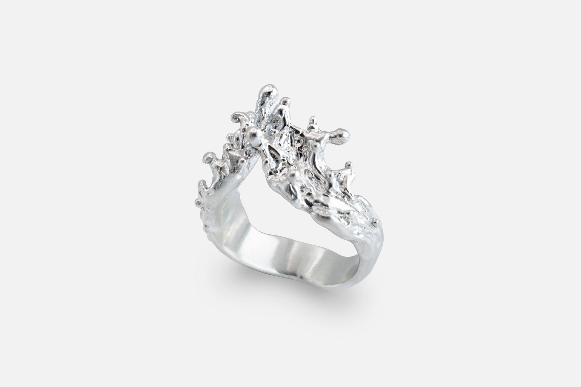 A silver ring with a sculptural, textured top, like waves of the sea rising to meet, photographed on a clean light gray background.