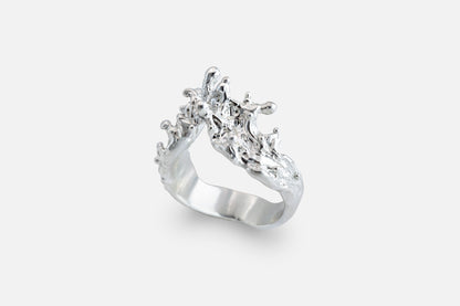 A silver ring with a sculptural, textured top, like waves of the sea rising to meet, photographed on a clean light gray background.