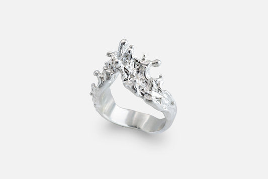 A silver ring with a sculptural, textured top, like waves of the sea rising to meet, photographed on a clean light gray background.