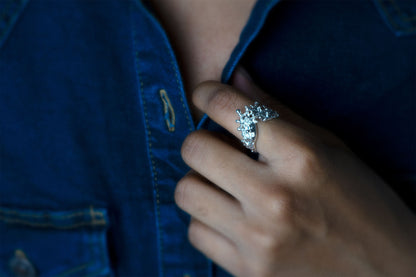 A close-up shot of a person wearing a silver ring with a sculptural, textured top, like waves of the sea rising to meet, pulling open a dark blue denim shirt.