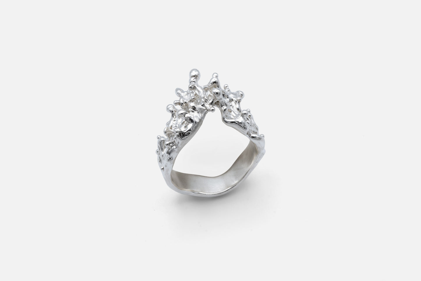 A silver ring with a sculptural, textured top, like waves of the sea rising to meet, photographed on a clean light gray background.