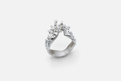 A silver ring with a sculptural, textured top, like waves of the sea rising to meet, photographed on a clean light gray background.